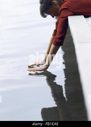 Woman lying on front hanging off pier touching surface of water, Copenhagen, Denmark Stock Photo