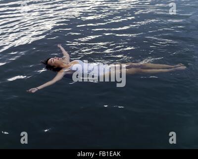 High angle view of woman floating on back in water arms outstretched looking up Stock Photo