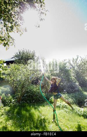 Front view of mature woman in garden standing on one leg squirting water into air with hosepipe Stock Photo