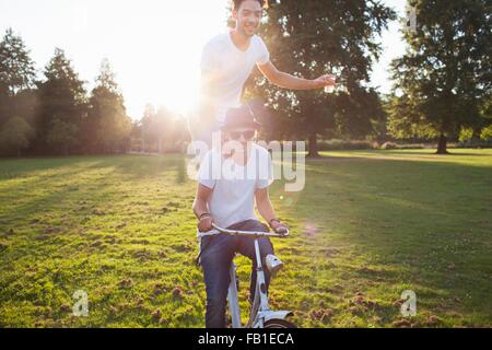 Party going man arriving in park standing on back of bicycle at sunset Stock Photo