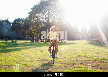 Young couple having fun on bicycle at sunset party in park Stock Photo