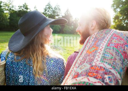 Rear view of romantic young couple carrying rug for picnic in park