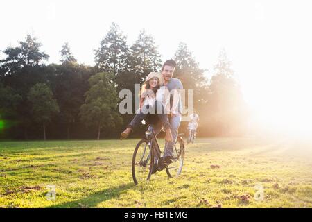 Young woman on handlebars of boyfriends bicycle at party in park Stock Photo