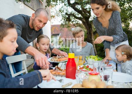 Father and teenage girl helping children at garden barbecue table Stock Photo