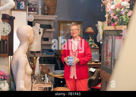 Portrait of mature woman holding china pot in vintage shop Stock Photo