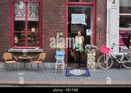Young female customer with jug and lamp outside vintage shop Stock Photo