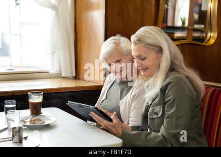 Mother and daughter sitting together in cafe, looking at digital tablet Stock Photo
