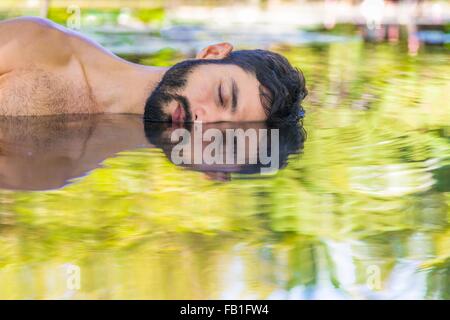 Bearded young man lying on side in water, illusion of mirror image, Taiba, Ceara, Brazil Stock Photo