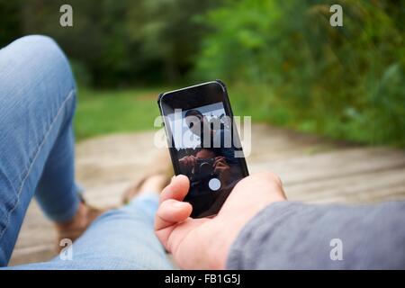 Heterosexual couple sitting outdoors, using smartphone, low section Stock Photo