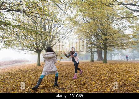 Two young girls playing, throwing leaves, in forest, autumn