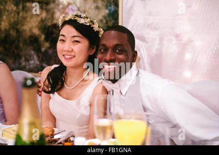 Bride and bridegroom at wedding reception sitting side by side looking at camera smiling Stock Photo