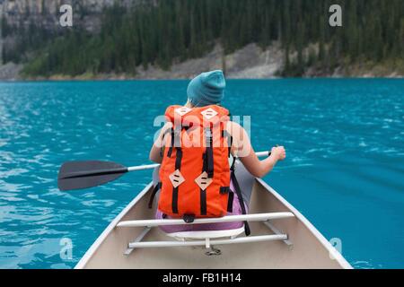 Rear view of mid adult woman with orange colour backpack paddling canoe, Moraine lake, Banff National Park, Alberta Canada Stock Photo