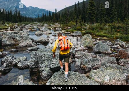 Rear view of mid adult man carrying backpack walking on rocky riverbed, Moraine lake, Banff National Park, Alberta Canada