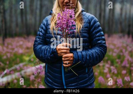 Cropped view of mid adult woman wearing padded coat holding wildflowers, Moraine lake, Banff National Park, Alberta Canada