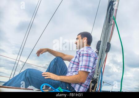 Low angle side view of young man on sailboat looking away smiling Stock Photo