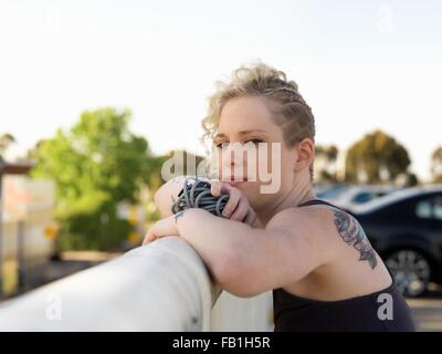 Portrait of young woman holding skipping rope leaning against urban railing Stock Photo