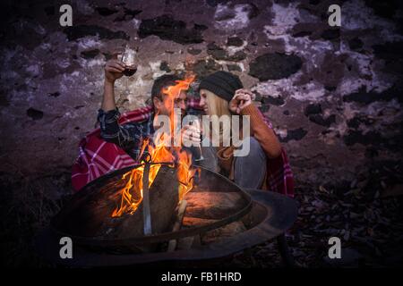 Romantic mature couple wrapped in blanket in front of campfire at night Stock Photo