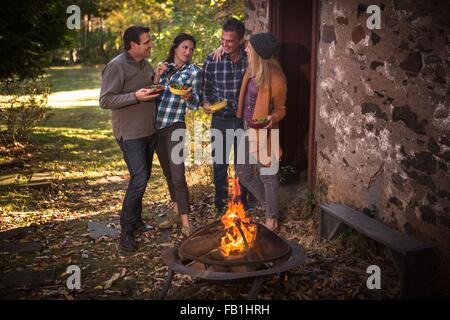 Two mature couples eating in front of campfire in garden Stock Photo