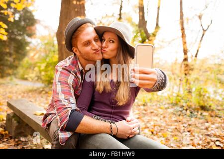 Young couple on bench taking smartphone selfie in autumn forest Stock Photo