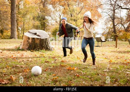 Young couple running after soccer ball in autumn park Stock Photo