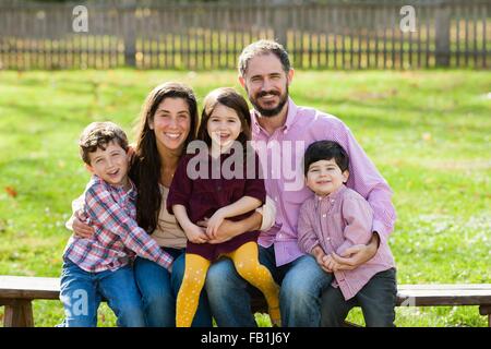 Family sitting on bench together looking at camera smiling Stock Photo