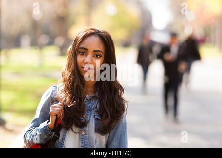 Portrait of young woman with long brown hair wearing denim jacket looking at camera smiling