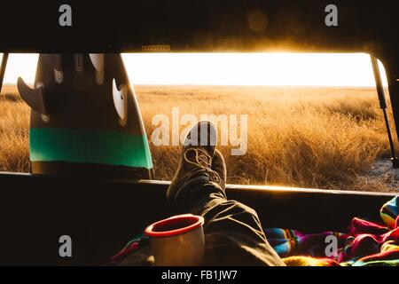 Male surfer with feet up in back of jeep at sunset, San Luis Obispo, California, USA Stock Photo