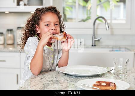 Girl at kitchen counter eating toast looking at camera Stock Photo
