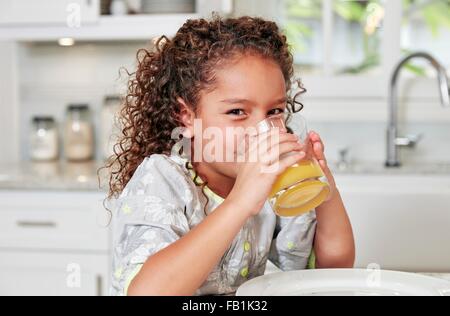 Girl at kitchen counter drinking orange juice looking at camera Stock Photo