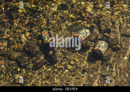 Three empty beer bottles discarded on the bed of a freshwater river. Metaphor environmental river pollution, Clean Up Britain campaign. Stock Photo