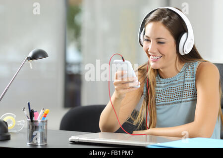 Girl listening to the music with a smartphone and headphones in her desktop at home Stock Photo