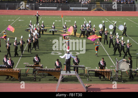 In full uniform and playing their musical instruments, a multiracial high school marching band performs on the field at a countywide band competition in Mission Viejo, CA. Note conductor in foreground. Stock Photo
