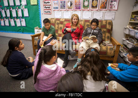 An elementary school teacher holds a reading seminar for her Hispanic students in the corner of her classroom in San Clemente, CA. Note posters describing reading goals and book nook at right. Stock Photo