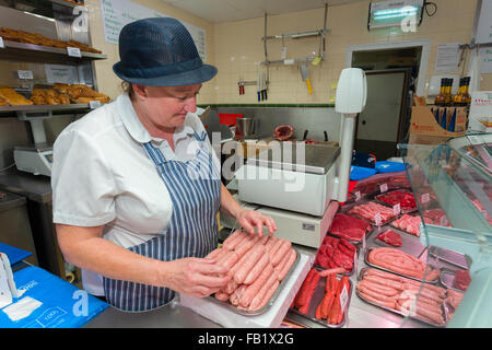 A woman stacking sausages in a butchers shop ready to be put on display for sale Stock Photo