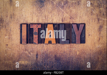 The word 'Italy' written in dirty vintage letterpress type on a aged wooden background. Stock Photo