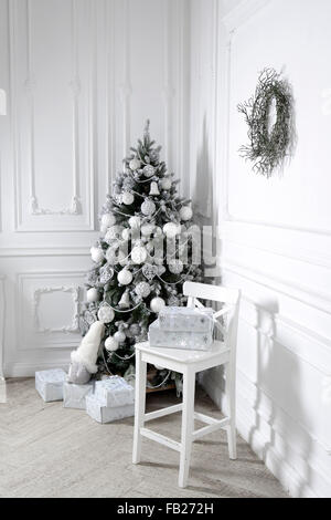 Beautiful holiday decorated room with Christmas tree with presents under it. Christmas tree decorated by artificial flowers and Stock Photo