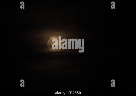 A full moon peeks out among wispy clouds in a pitch black sky Stock Photo