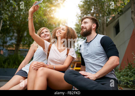 Three young friends taking a selfie with cellphone. Multiracial group of young people having fun together while sitting outdoors Stock Photo