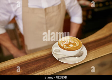 Close up of cup of fresh coffee on the wooden counter with a barista standing by Stock Photo