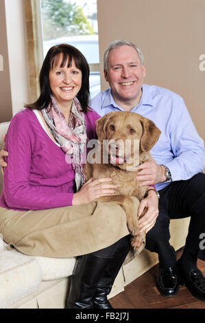 A middle age couple sat on a sofa hugging their dog Stock Photo