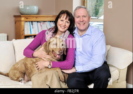 A middle age couple sat on a sofa hugging their dog Stock Photo
