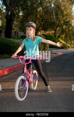 A tween girl bicyclist signals a left turn using her arm on a street in Lake Forest, CA MODEL RELEASE Stock Photo