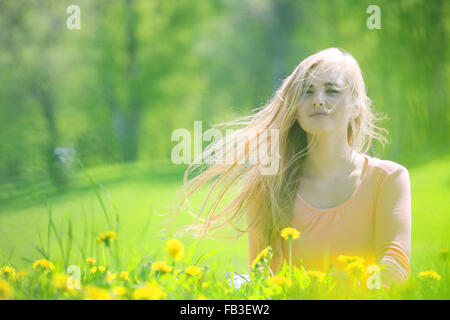 Beautiful young woman laying in spring park with dandelion flowers Stock Photo