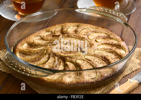 Homemade apple and cinnamon cake in glass dish with two cups of tea in the back, photographed with natural light Stock Photo