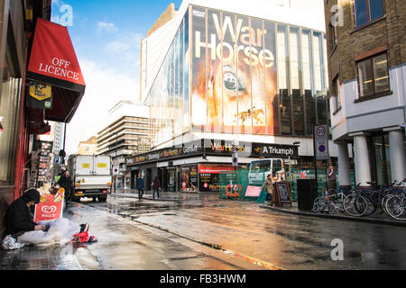 Homeless man huddled under awning in wet London street outside the New London Theatre on Drury Lane, which is showing War Horse Stock Photo