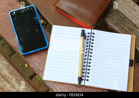 background of notebook and pen with mobile phone and wallet on the brown bench during daytime Stock Photo