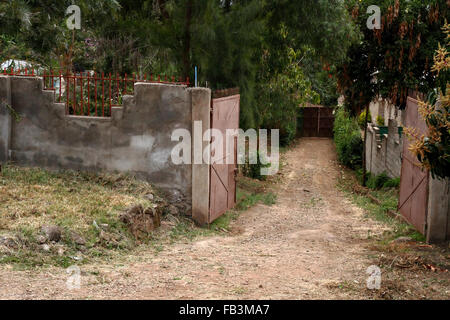 Looking down a path through a walled compound with two solid metal gates Stock Photo