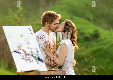 Couple covered in paint kisses behind the sketchbook Stock Photo