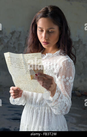 Young woman in antique lace dress reading a sad letter Stock Photo