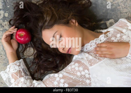 Stunning young woman in white lace dress lying on the floor with a red apple Stock Photo